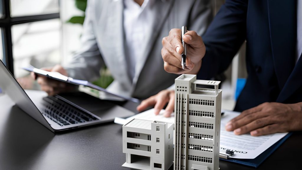 Businesspeople Review a Desk-scale Model of White Office Buildings During a Planning Meeting, with a Laptop Nearby. - Hola Mty