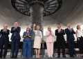 Group of Formally Dressed Dignitaries Standing in a Line on a Stage, Applauding, with a Large Circular Sculpture Behind Them Under a Modern Canopy. - Hola Mty