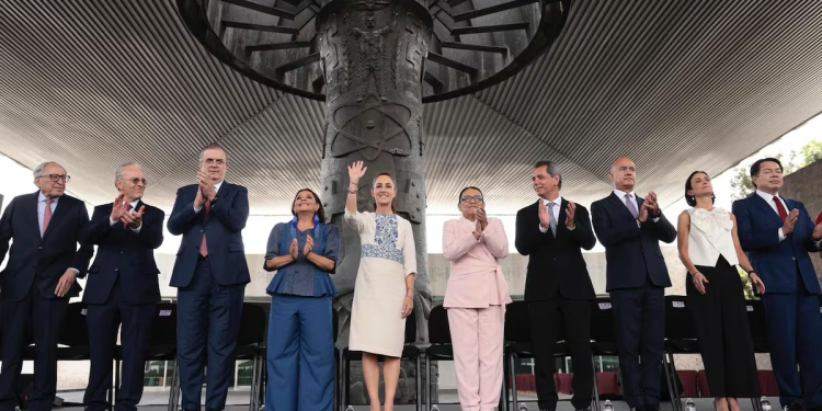 Group of Formally Dressed Dignitaries Standing in a Line on a Stage, Applauding, with a Large Circular Sculpture Behind Them Under a Modern Canopy. - Hola Mty