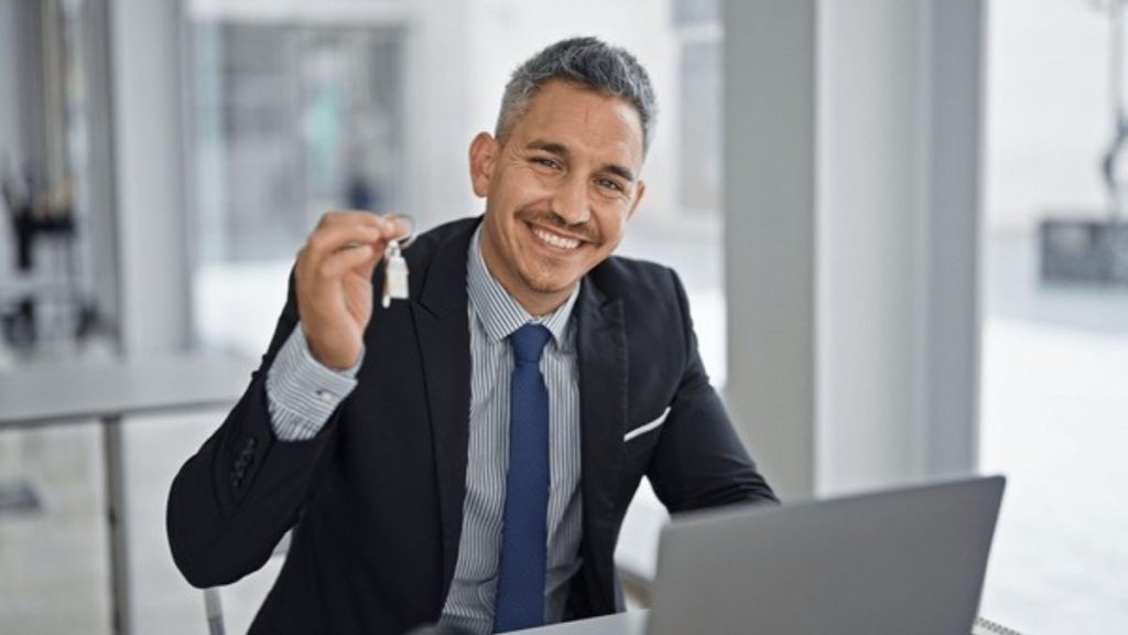 Contrato-quantium-desarrollos-era-inmobiliaria-preventas - Hola Mty Smiling Man in a Dark Suit Holds Up a Set of Keys at His Desk with a Laptop in a Bright Office. - Hola Mty