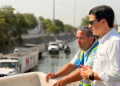 Two Men Overlook a Canal Worksite; One Wears a White Shirt and Sunglasses, the Other in a Blue Safety Vest, with Trucks in the Background. - Hola Mty