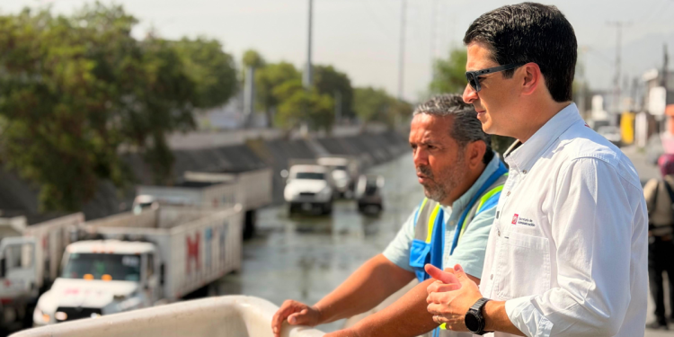 Canal-medular-aztlan-es-limpiado - Hola Mty Two Men Overlook a Canal Worksite; One Wears a White Shirt and Sunglasses, the Other in a Blue Safety Vest, with Trucks in the Background. - Hola Mty