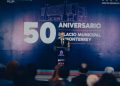 Speaker in a Suit Delivers a Speech at a Podium During Monterrey's 50th Anniversary of the Municipal Palace, with a Large '50 Aniversario' Backdrop Behind Him. - Hola Mty