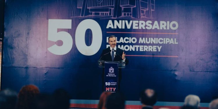 Speaker in a Suit Delivers a Speech at a Podium During Monterrey's 50th Anniversary of the Municipal Palace, with a Large '50 Aniversario' Backdrop Behind Him. - Hola Mty